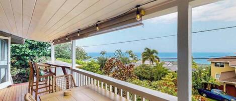 Um deck de madeira com mesa e cadeiras, com vista para uma área residencial e o oceano.