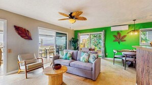 A living room with a sofa, a round coffee table, a ceiling fan, and a green accent wall. - NEW Kona Family Home and Ohana with Bay Sunsets (Kailua-Kona)