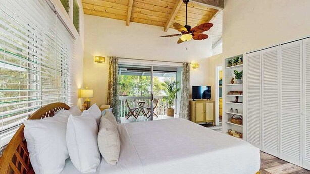 A bedroom with a bed, a ceiling fan, a TV, a balcony with a table, and a wardrobe. - NEW Kona Family Home and Ohana with Bay Sunsets (Kailua-Kona)