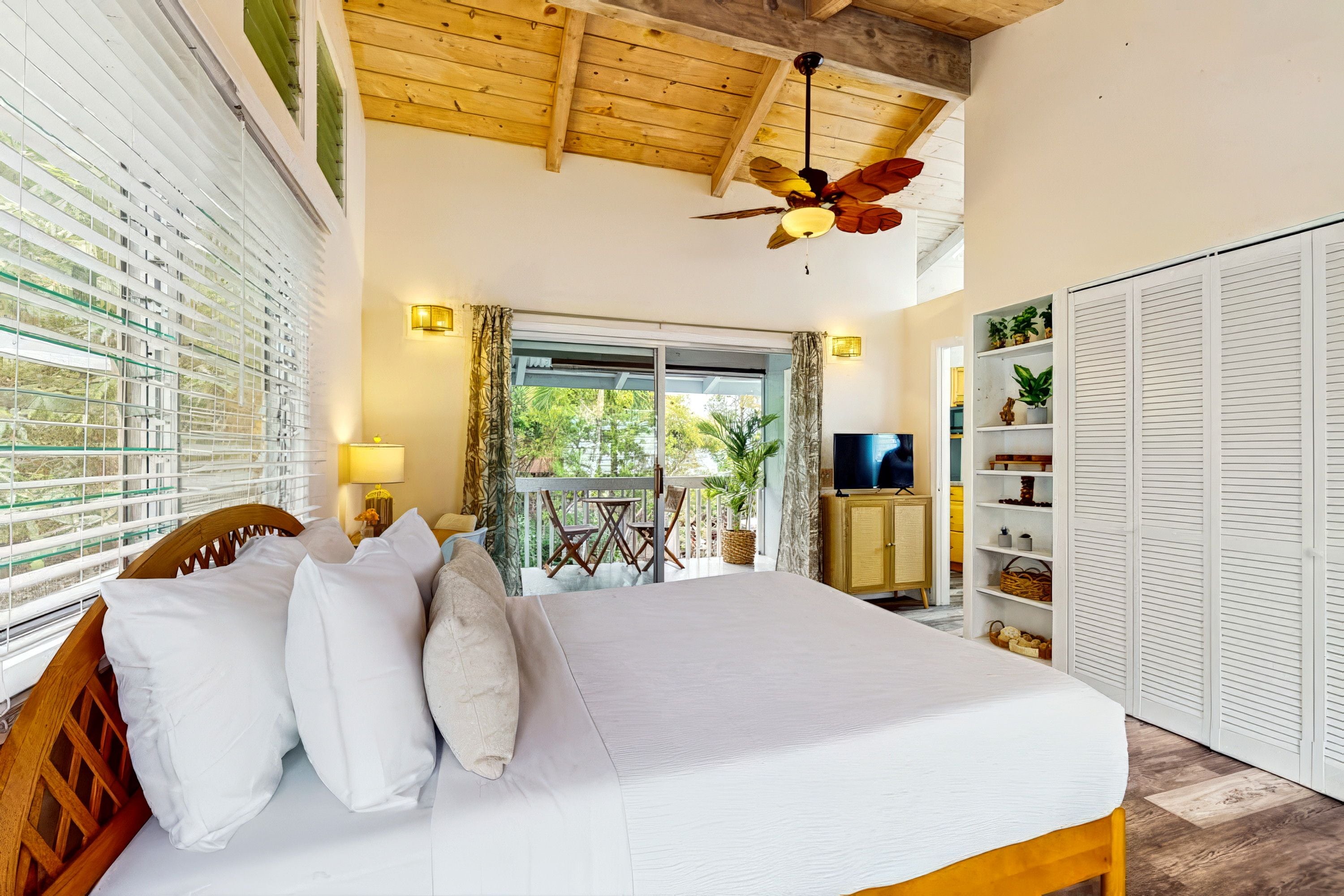 Een slaapkamer met een bed, een televisie, een kledingkast en een balkon met uitzicht op groen.