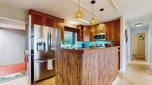 A modern kitchen with wooden cabinets, stainless steel appliances, and a central island. - NEW Kona Family Home and Ohana with Bay Sunsets (Kailua-Kona)