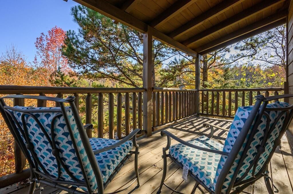 Een overdekt terras met twee stoelen en een tafel, omgeven door een houten terras en een balustrade.
