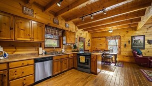A wooden cabin interior with a kitchen, dining area, and a fireplace. - Bear Hug (Pigeon Forge)