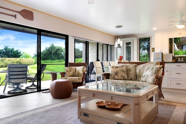 A spacious living area with a glass coffee table, comfortable seating, and a view of a lush garden through large sliding doors. - Keauhou Punahele Golf/Beach Condo - Pool, Hot Tub, WIFI, Kitchen, BBQ, Laundry (Kailua-Kona)