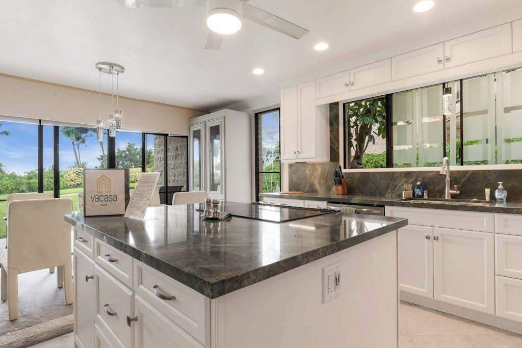 A modern kitchen with white cabinets, a granite countertop, and a view of greenery outside.