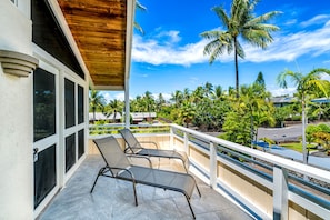 Ein Balkon mit zwei Liegestühlen, Holzboden und Blick auf Palmen und einen Pool.
