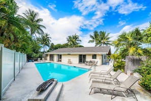 A swimming pool with lounge chairs, a building with a patio, and palm trees. - Kona He'eia Haven Group Combo Retreat- Private Pool, Kitchen/Dining, Near Beach (Kailua-Kona)