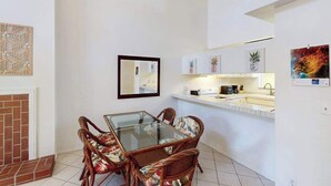 Un comedor con mesa de vidrio y sillas de mimbre, una cocina con gabinetes blancos y una chimenea.