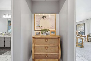 Ein Flur mit einem Rattan-Kommode, gerahmten Kunstwerken und einem Blumentopf.