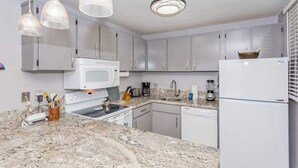 Una cocina moderna con armarios blancos, una estufa blanca, un microondas, un lavaplatos y un refrigerador.