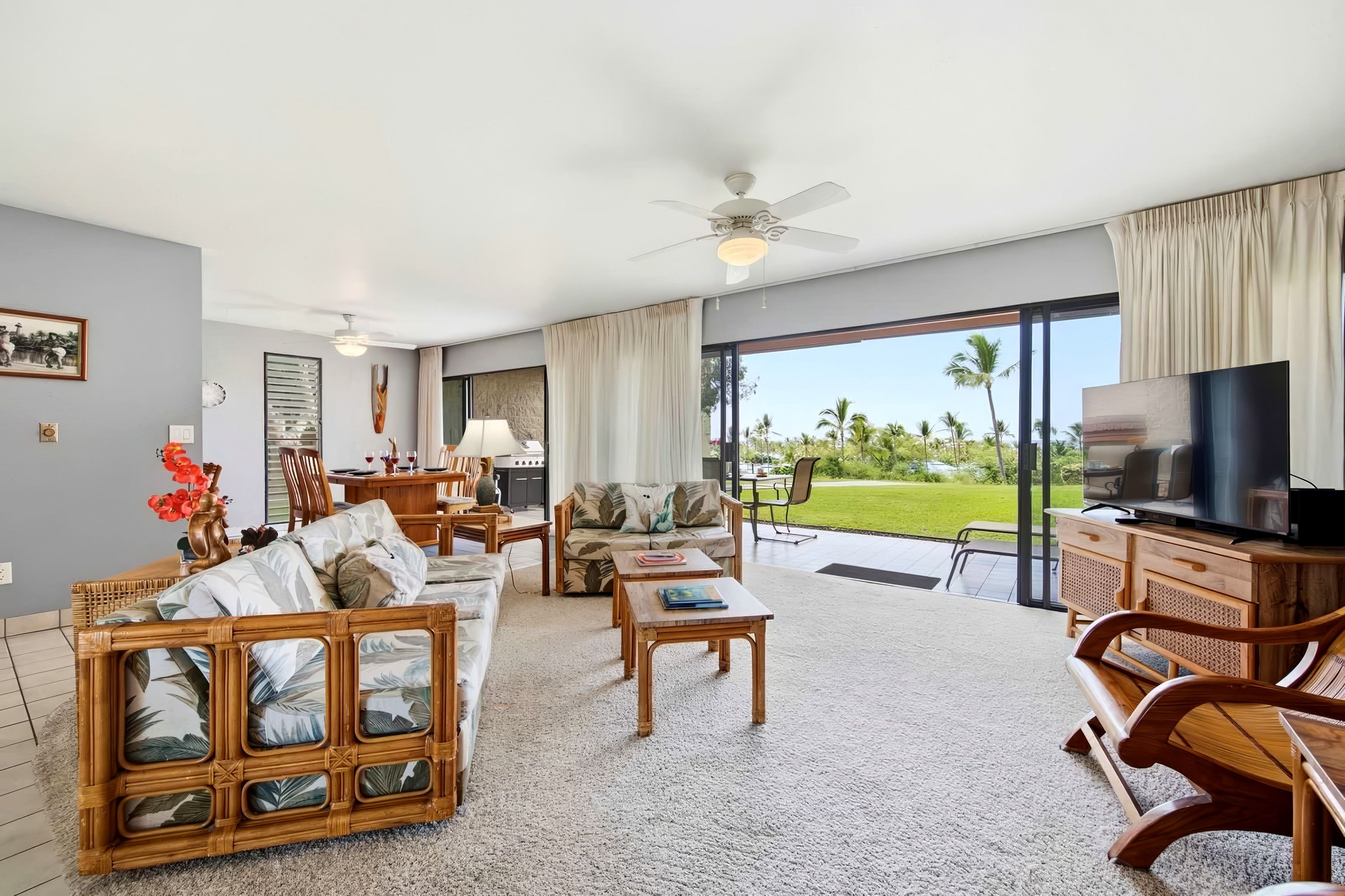 A spacious living area with a large television, comfortable seating, and a view of a lush garden.