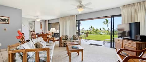 A spacious living area with a large television, comfortable seating, and a view of a lush garden.