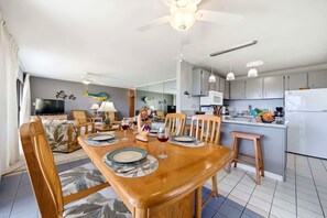 Une cuisine moderne dotée d’un îlot central, d’une table à manger en bois pouvant accueillir six personnes et d’un ventilateur de plafond.