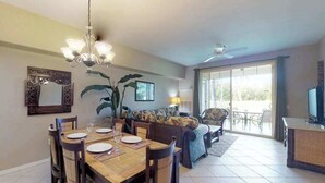 A dining area with a wooden table, chairs, and a chandelier. There is a sofa and a television in the living area. - *NEW* Fall Sale Garden-Level Fairway Stay by Kings' Shops and A-Bay (Waikoloa)