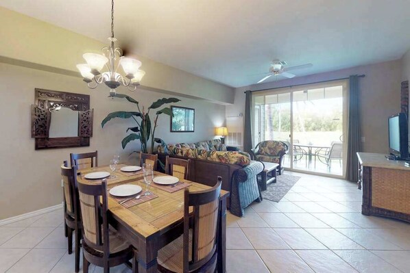 A dining area with a wooden table, chairs, and a chandelier. There is a sofa and a television in the living area. - *NEW* Fall Sale Garden-Level Fairway Stay by Kings' Shops and A-Bay (Waikoloa)