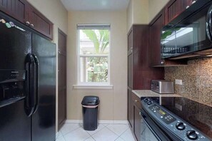 A compact kitchen with a refrigerator, microwave, stove, and a window with a view of greenery. - *NEW* Fall Sale Garden-Level Fairway Stay by Kings' Shops and A-Bay (Waikoloa)