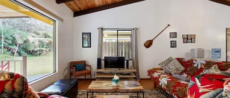 A cozy living room with a wooden ceiling, a television, a sofa, and a dining table.