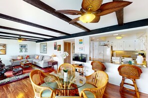 A spacious living area with a dining table surrounded by wicker chairs, a ceiling fan, and a television. - *NEW* Top Floor Kona Coast Views for a Family of Four (Kailua-Kona)