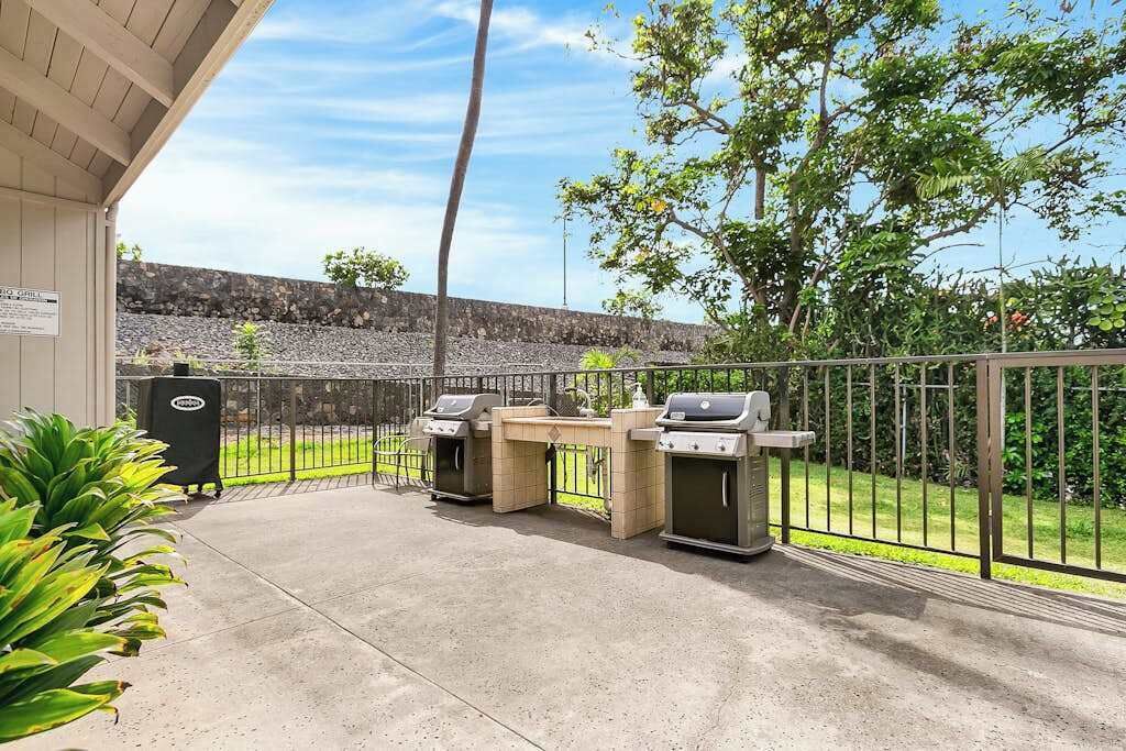 Una terrazza esterna con due barbecue, un pavimento in cemento, una recinzione metallica e un muro in pietra sullo sfondo.