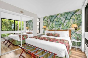Quarto com uma cama grande, duas mesas de cabeceira, um banco, uma janela e parede com padrão de folhagem tropical.
