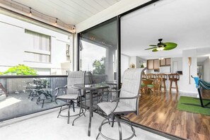 A modern interior with a dining area, kitchen, and a balcony with outdoor furniture. - Kailua Bay Casa Tropical Kona Condo- Pool, Hot Tub, AC, WD- Walk to Beach Fun (Kailua-Kona)