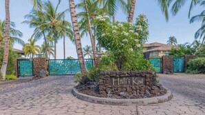 Entrada d'un resort tropical amb un rètol que diu 'Hali Kai', palmeres i una paret de pedra.