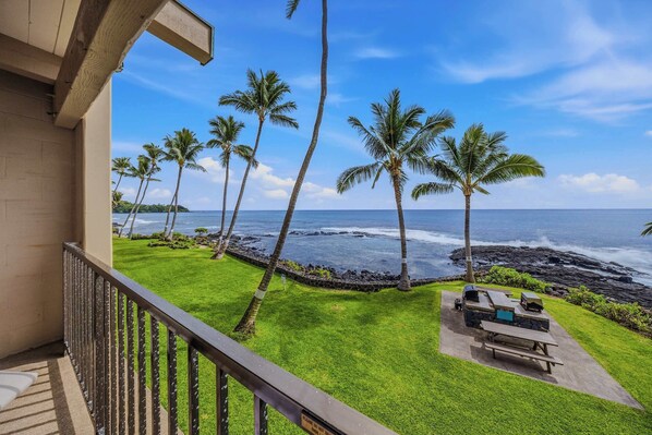 A balcony with a view of the ocean, palm trees, and a barbecue area. - Oceanfront 2bd Kona Bali Kai 220- Pool, Hot Tub, Laundry, Kitchen, Beach Access (Kailua-Kona)