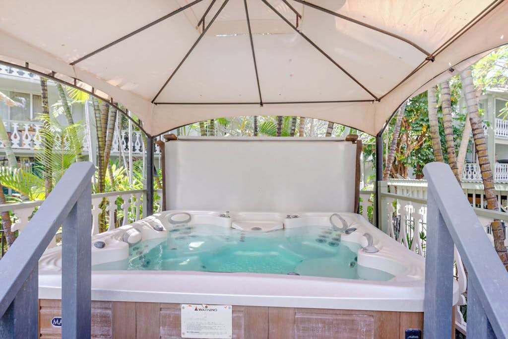 A hot tub under a canopy with a view of palm trees and a white fence.