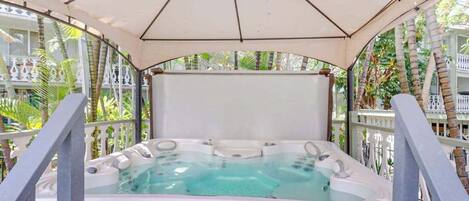 A hot tub under a canopy with a view of palm trees and a white fence.