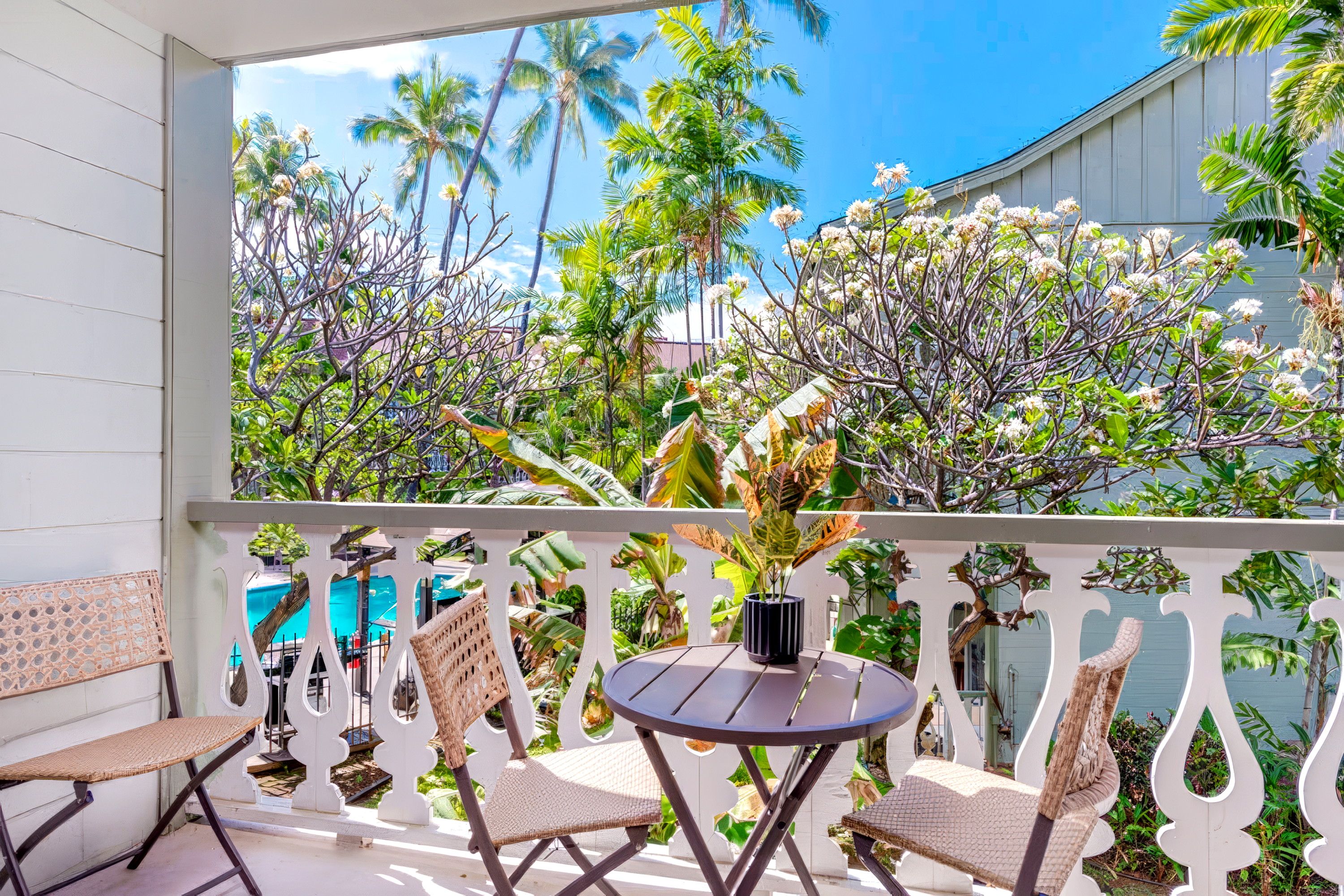 A balcony with a white railing, two wicker chairs, a small round table, and a potted plant.