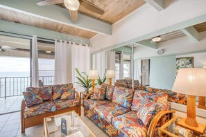 Una habitación con sofá, una mesa y una lámpara. Hay cortinas y un ventanal.