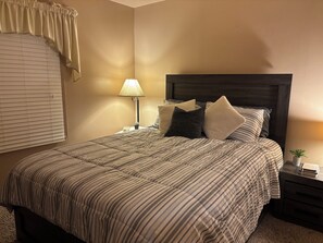 A neatly made bed with striped bedding, a bedside lamp, and a small plant on the nightstand. - Upper Bi-Level Three Bedroom Home with a Beautiful Deck in South Indy (indianapolis)