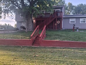 A residential property with a wooden staircase leading to a deck, a large tree, and a birdbath. - Upper Bi-Level Three Bedroom Home with a Beautiful Deck in South Indy (indianapolis)