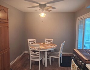 A dining area with a round table, four chairs, a ceiling fan, and a window with blinds. - Upper Bi-Level Three Bedroom Home with a Beautiful Deck in South Indy (indianapolis)