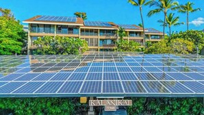 Un hotel con varios pisos, paneles solares en el techo y abundante vegetación alrededor.