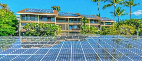 Un hôtel à étages, doté de panneaux solaires sur le toit et entouré d’une végétation luxuriante.