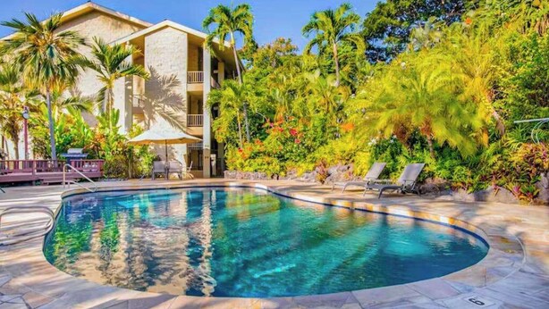 Una piscina con agua cristalina, rodeada de palmeras y un edificio con balcones.