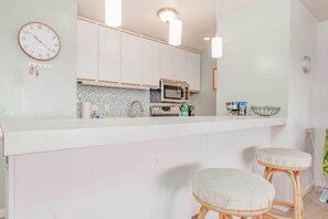 A kitchen with white cabinets, a microwave, and a clock on the wall. - New Third-Floor Kona Views, Walk to Pier and Market (Kailua-Kona)