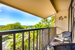 A balcony with a view of the ocean and palm trees, a chair, and a wall-mounted decorative item. - New Third-Floor Kona Views, Walk to Pier and Market (Kailua-Kona)