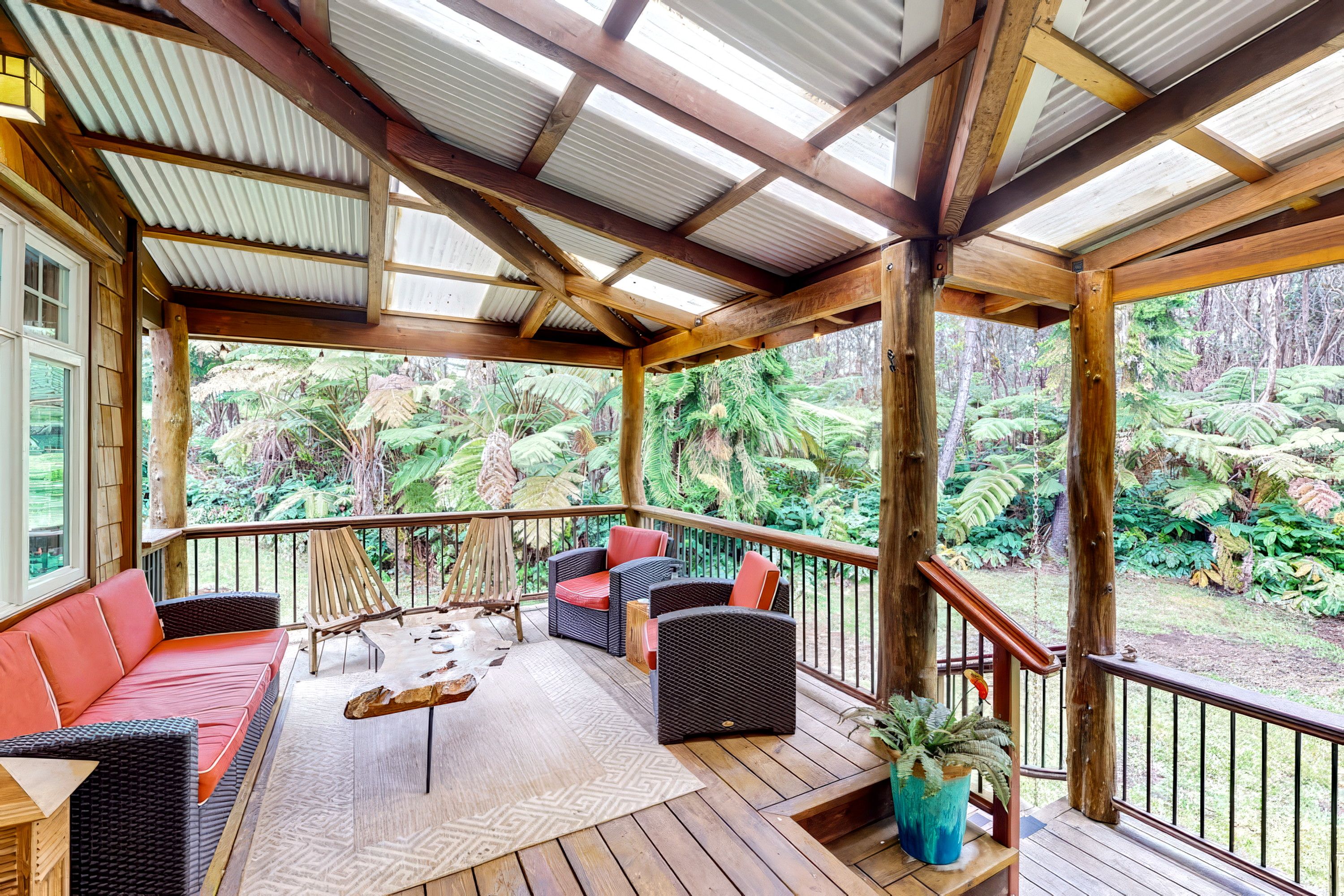 A covered outdoor area with wooden flooring, seating arrangements, and a view of a lush garden.