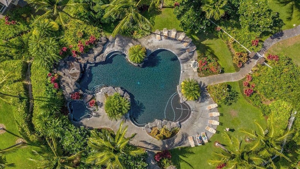 An aerial view of a resort with a central swimming pool, surrounded by palm trees and a stone deck with lounge chairs. - *New* Fall Sale Mauna Lani Condo Near Beach Path with Waterfall Pool and Tennis (Kamuela)