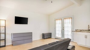 Ein modernes Wohnzimmer mit einer Couch, einem Flachbildfernseher, einem grauen Schrank und einer Küchenzeile mit Arbeitsplatte und Schränken.