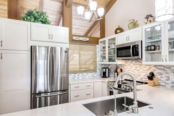 A modern kitchen with stainless steel appliances, white cabinetry, and a tiled backsplash.