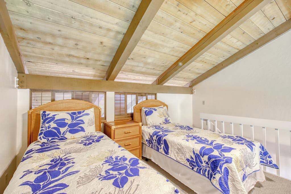 A bedroom with two beds, wooden ceiling beams, white walls, and a window with blinds.