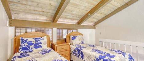 A bedroom with two beds, wooden ceiling beams, white walls, and a window with blinds.