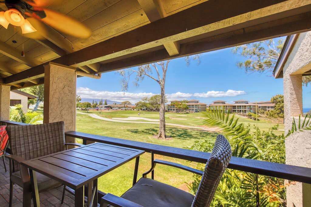 Un patio al aire libre con una mesa y sillas, vista a un campo de golf y un edificio al fondo.