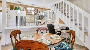 Een moderne keuken met witte kasten, roestvrijstalen apparatuur en een eethoek met een houten tafel en stoelen.