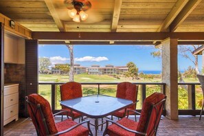 A covered outdoor seating area with a table and chairs, a ceiling fan, and a view of a golf course and buildings.