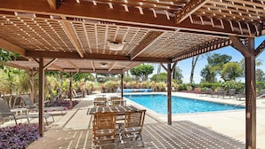 Een overdekt buitengebied met een zwembad, houten meubilair en een pergola.