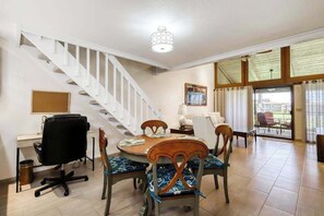 A dining area with a round table, four chairs, a black office chair, a white desk, a computer, and a staircase.
